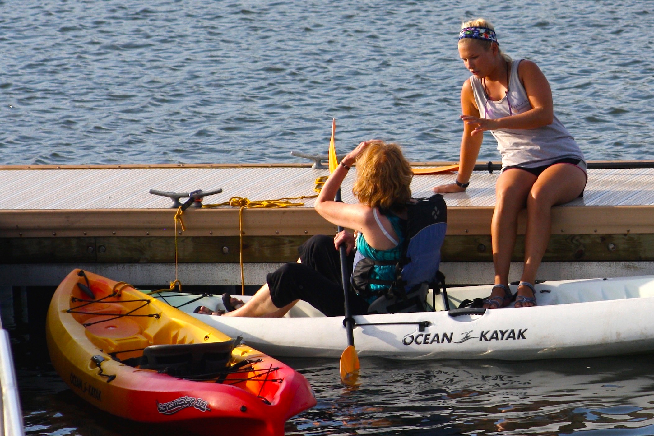 Learning to Kayak in Charleston, SC woman sitting on a dock teaching another woman about kayaking on the water in Charleston, SC